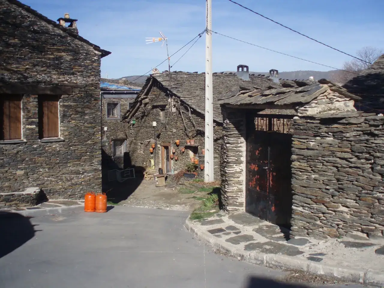 Casas de piedra con tejados de pizarra en un pueblo de la ruta negra Guadalajara. Dos bombonas naranjas esperan en la calle.