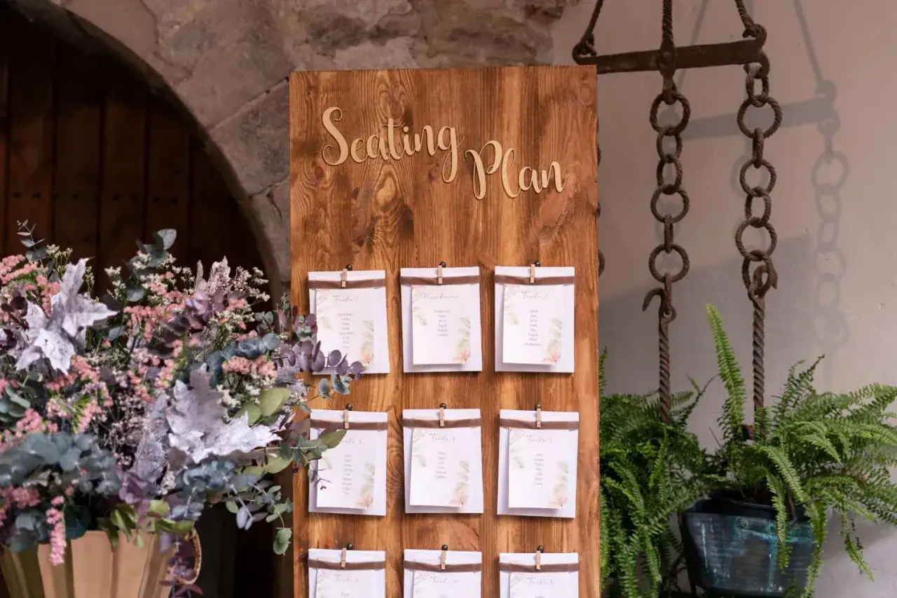 Un original seating plan boda en madera rústica, con tarjetas de invitados y un ramo de flores secas.
