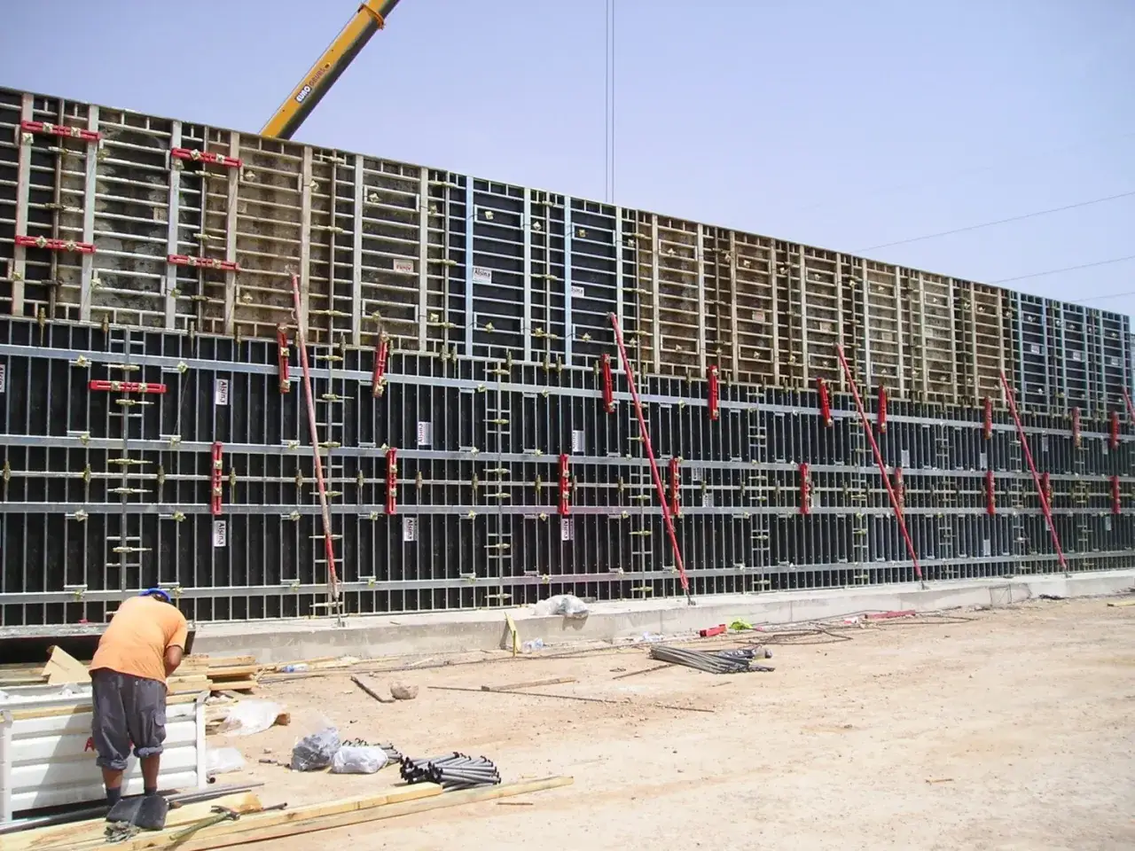 Trabajador supervisa el encofrar muro de gran tamaño, con estructura metálica y paneles negros, listo para el hormigón.