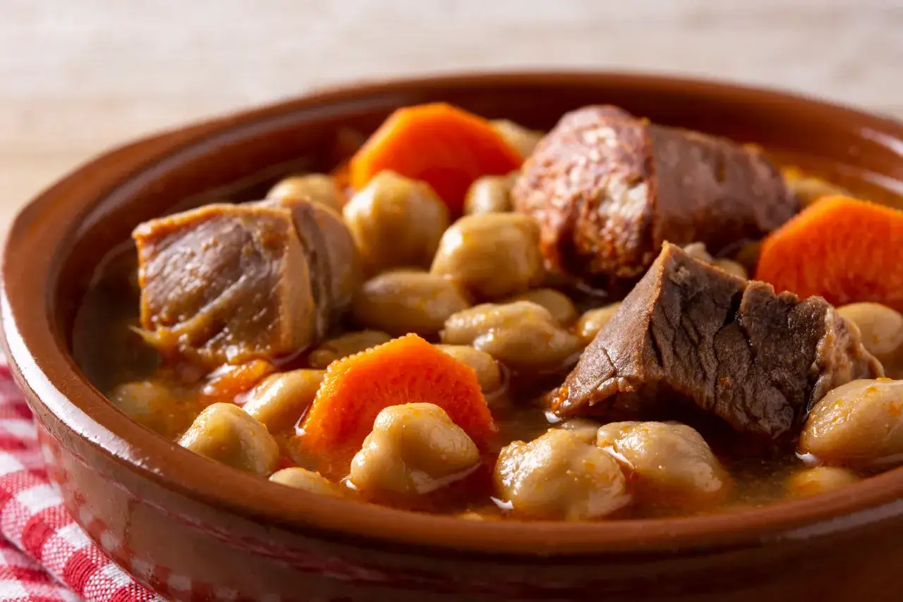 Un saporito cocido madrileño, perfetto per scoprire cosa mangiare a Madrid. Ceci, carne e carote in una ciotola di terracotta.