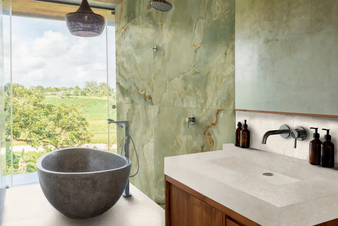 Bagno con vasca in pietra e lavabo integrato. L'altezza del rivestimento doccia in marmo verde crea un effetto scenografico.