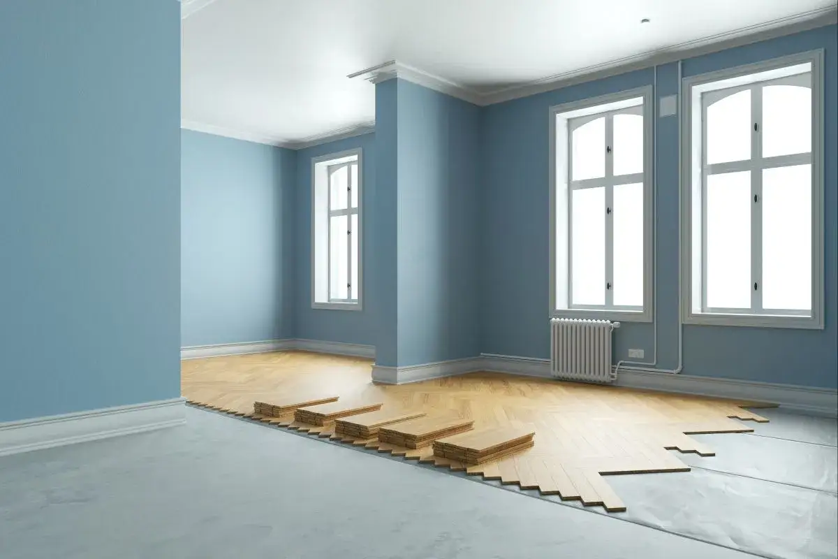 Stanno per essere posati nuovi materiali per pavimenti in legno in una stanza con pareti azzurre e grandi finestre.