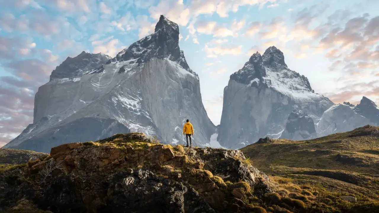 Un randonneur en jaune admire les pics majestueux lors d'une randonn&eacute;e argentine. Le ciel est parsem&eacute; de nuages roses et bleus.