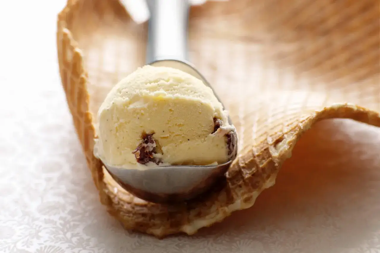 Ein Löffel cremiges Eis mit Rosinen und Rum ruht auf einem Waffelrand.