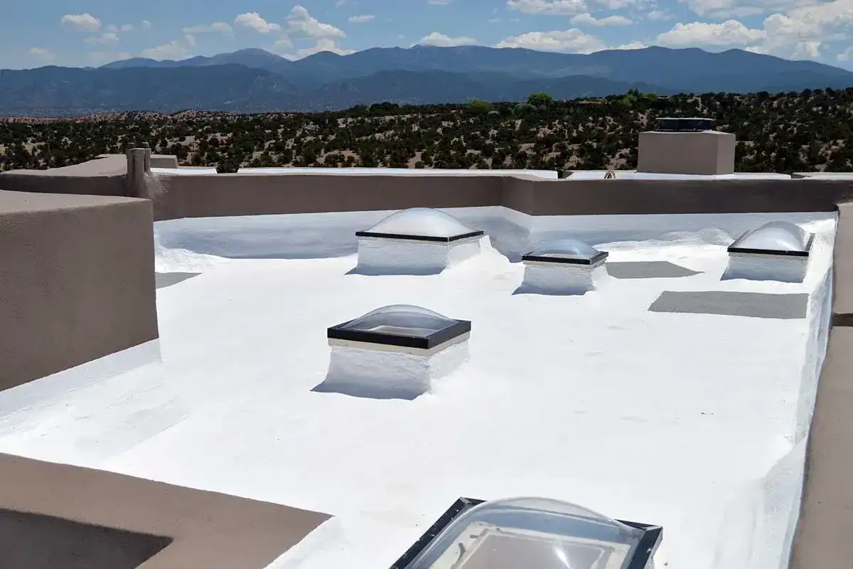 Un tejado blanco y plano con varias claraboyas, rodeado de monta&ntilde;as y vegetaci&oacute;n &aacute;rida bajo un cielo azul.