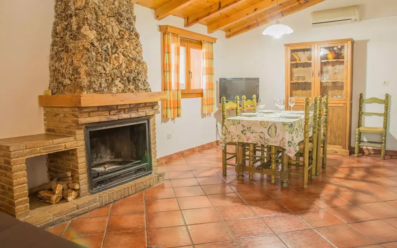 Acogedor sal&oacute;n con chimenea de piedra y ladrillo, mesa puesta y vitrina de madera. Un ejemplo de casas de campo sencillas y bonitas.