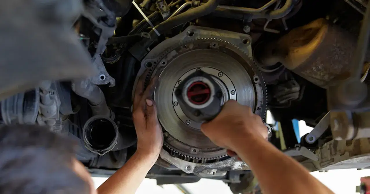 Mechanik dokonuje wymiany dwumasy w samochodzie, pracując przy skrzyni biegów.