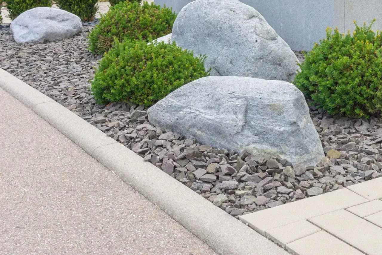 Am&eacute;nagement paysager moderne avec des rochers, des arbustes et une pose de bordure b&eacute;ton d&eacute;limitant une all&eacute;e.