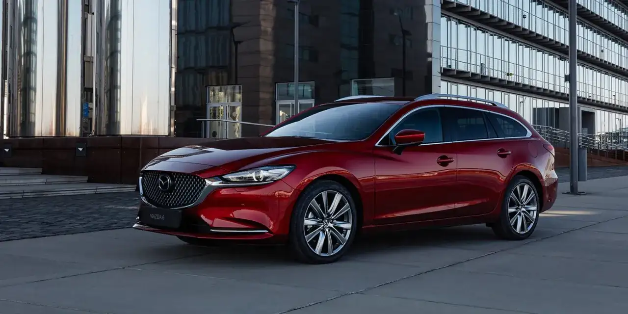 Czerwona Mazda 6 2.0 benzyna kombi zaparkowana przed nowoczesnym budynkiem.