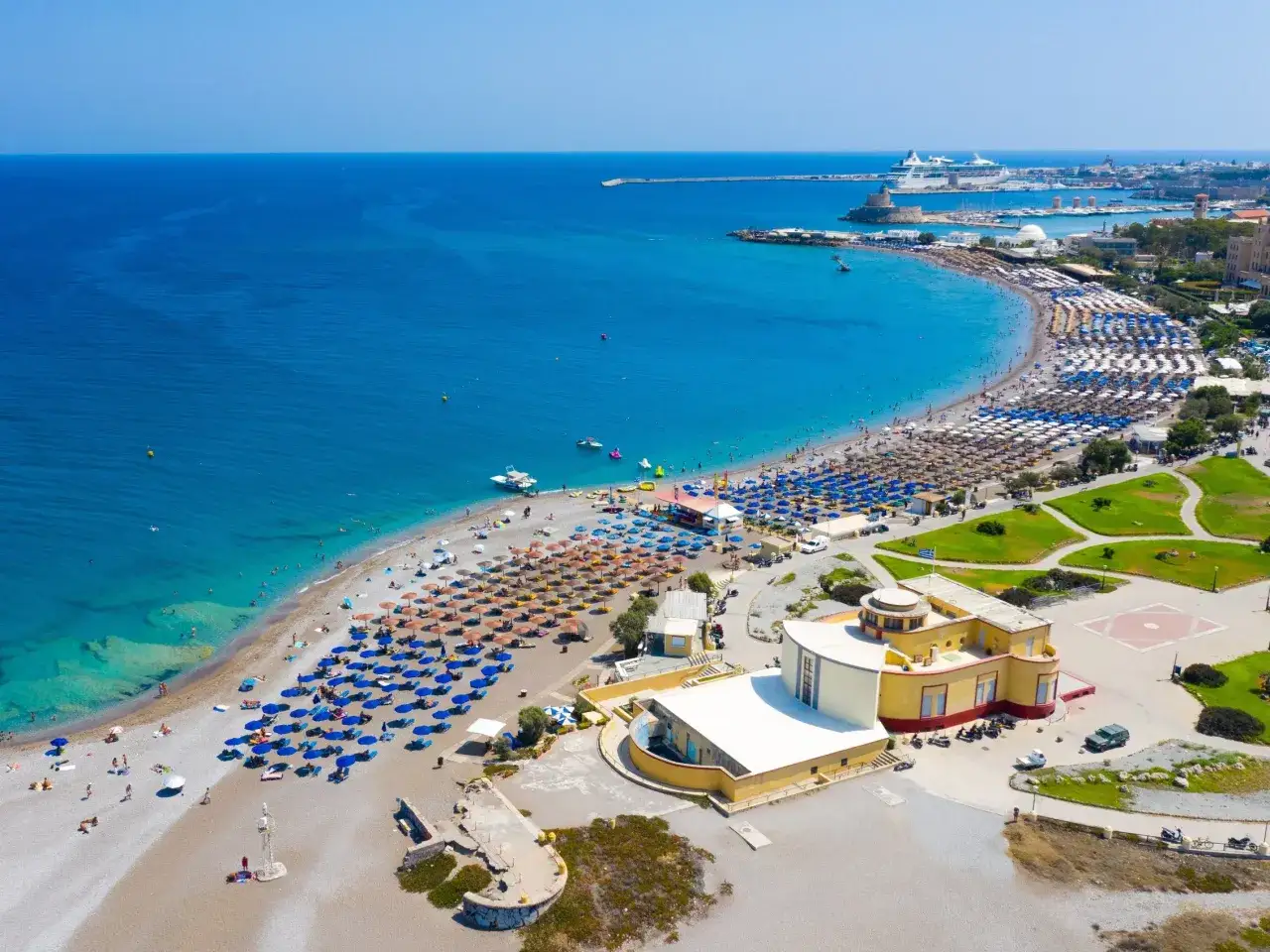 Rajskie wakacje all inclusive z niemowlakiem: plaża pełna leżak&oacute;w i parasoli, turkusowe morze, statki wycieczkowe w oddali. Idealne miejsce na rodzinny wypoczynek.
