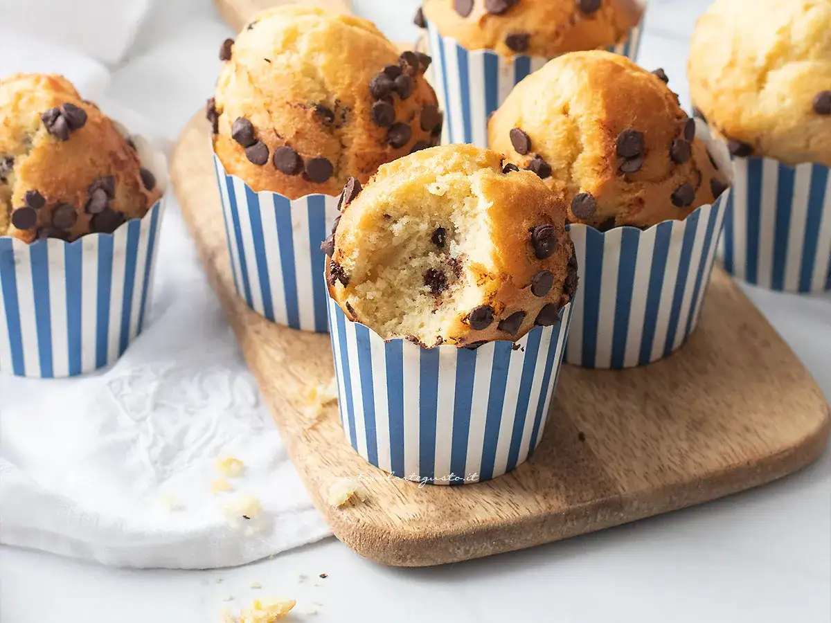 Muffin in friggitrice ad aria morbidissimi, con gocce di cioccolato, in pirottini a righe blu e bianche, uno è morso.