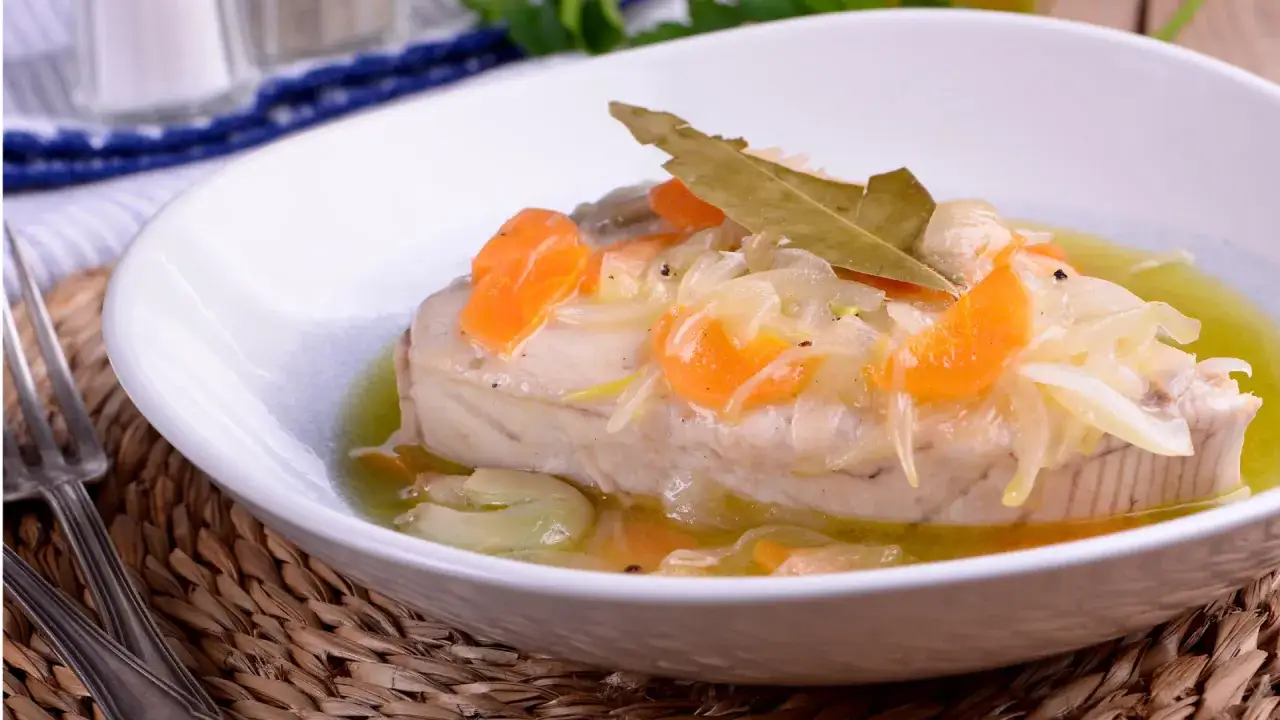 Delicioso atún en escabeche con zanahoria y cebolla, servido en un plato blanco sobre una base de mimbre.