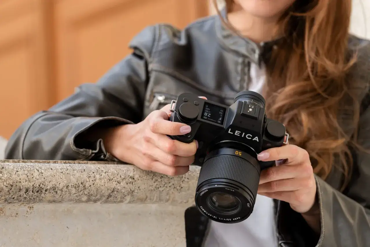 A person in a leather jacket holds a Leica camera, a testament to the question: are Leica cameras good?