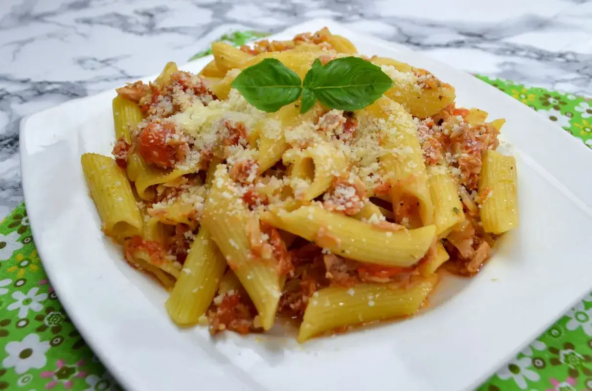 Penne z tuńczykiem i pomidorami, posypane parmezanem i udekorowane bazylią. Pyszne danie na szybki obiad.