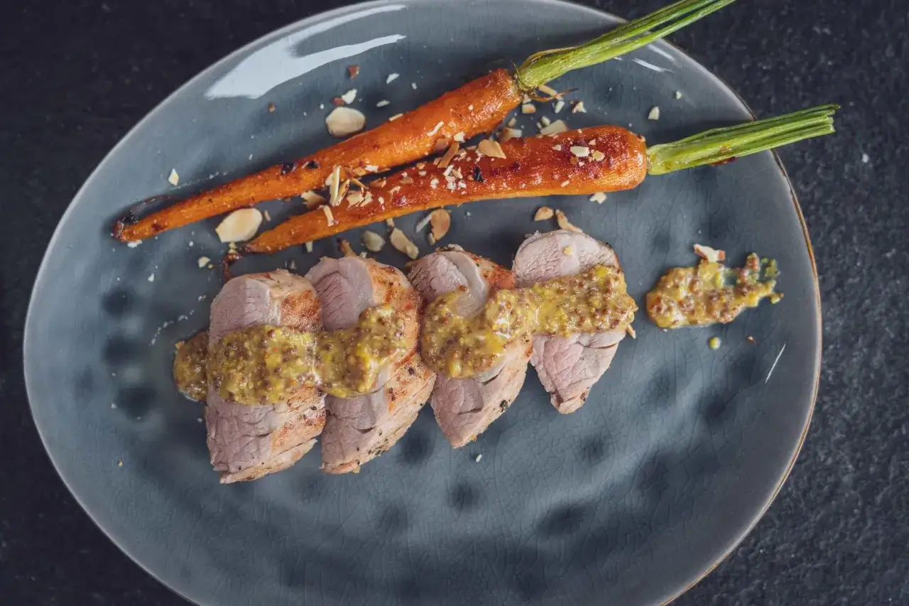Zartes **Schweinefilet grillen** mit Honig-Senf-Sauce und karamellisierten Karotten, bestreut mit Mandelsplittern.