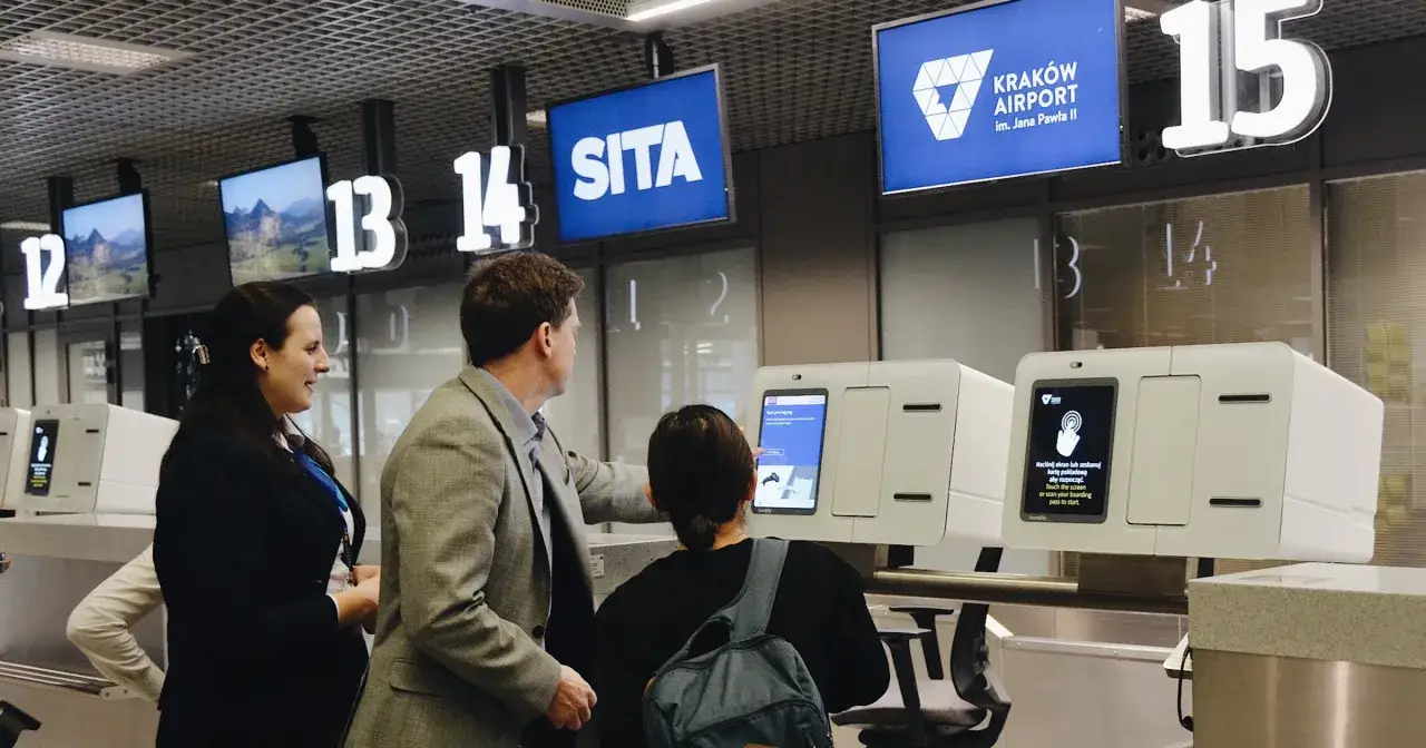 Osoby przy stanowisku odprawy na lotnisku Krak&oacute;w Airport uczą się, jak nadać bagaż na lotnisku, korzystając z ekran&oacute;w dotykowych.