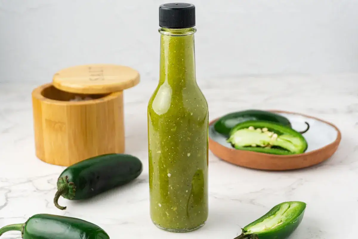 Butelka zielonego sosu, obok świeże jalapeno ile shu i drewniany pojemnik z solą.