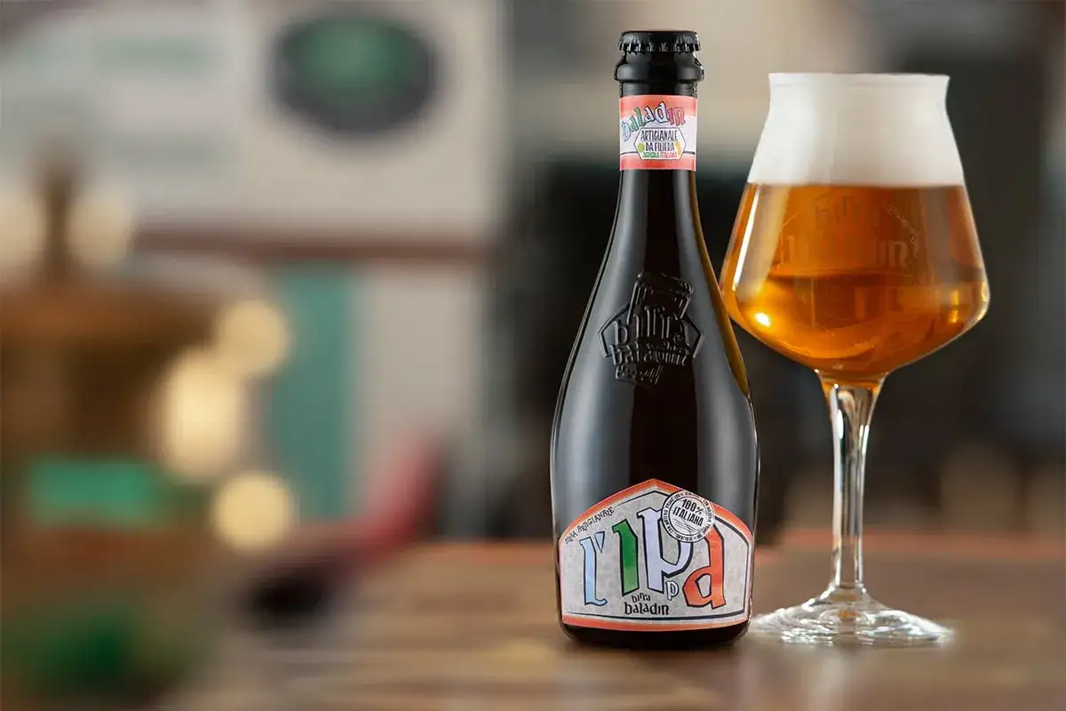 Una bottiglia e un bicchiere di italian pale ale, birra Baladin, su un tavolo di legno.