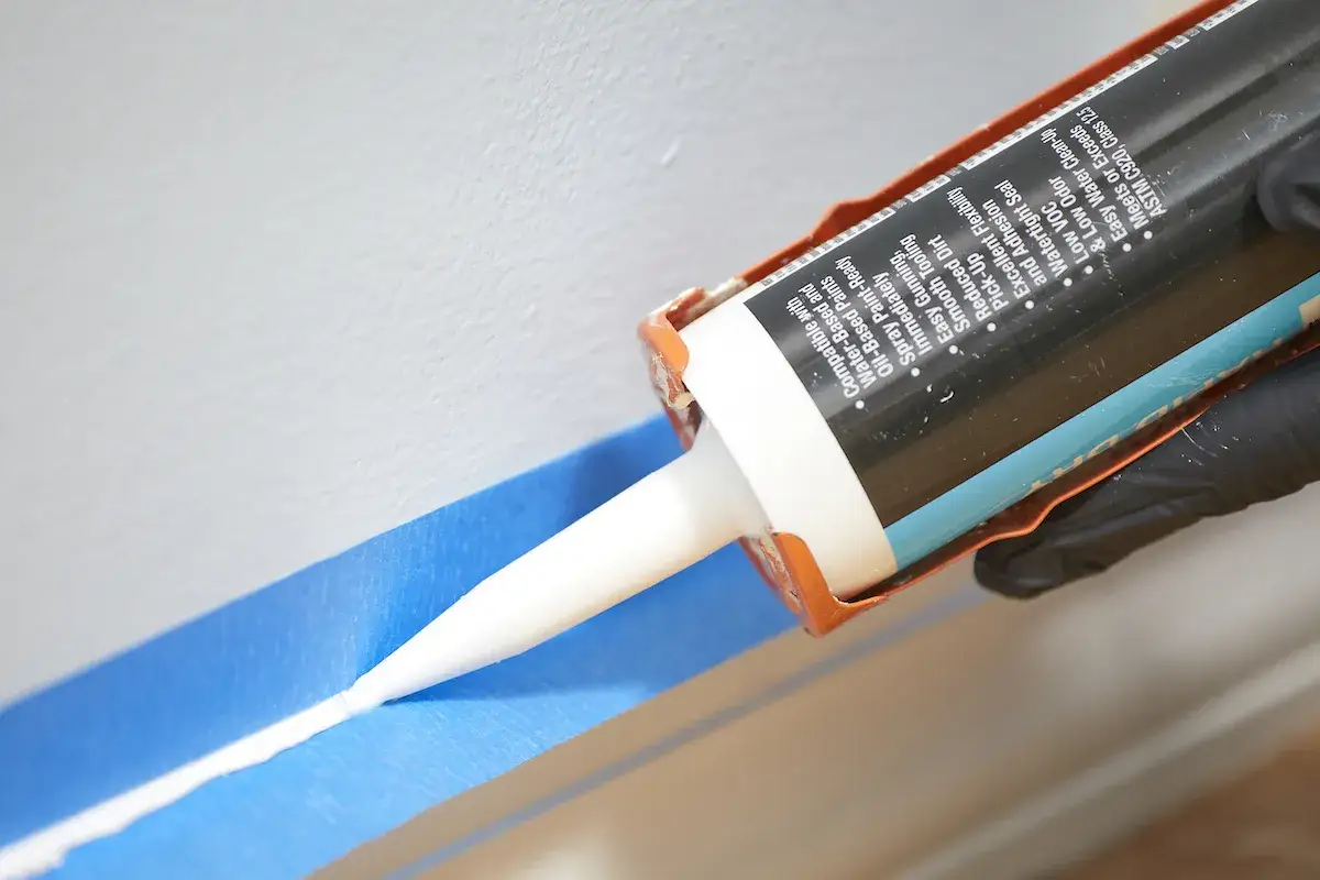 Applying a bead of caulk along blue painter's tape, demonstrating how to caulk for a clean finish.