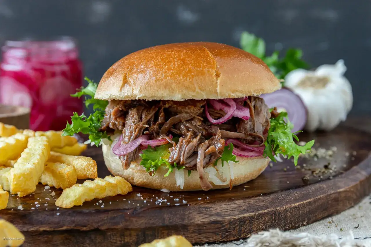 Saftiger pulled beef burger mit roten Zwiebeln und knackigem Salat, serviert mit Pommes.