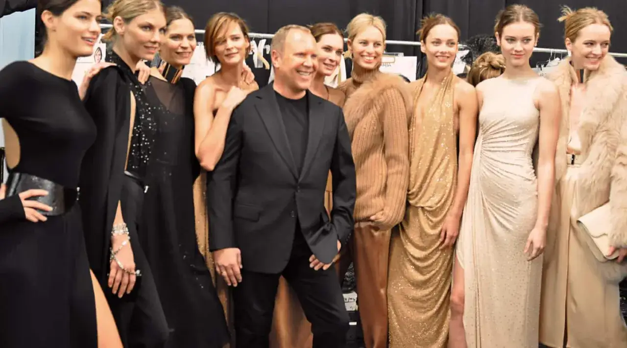 Michael Kors, znany z luksusowych ubrań i akcesoriów, pozuje z modelkami w złotych i czarnych kreacjach.