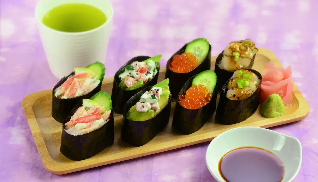 Różnorodne gunkan sushi z krabem, awokado, ikrą łososia i przegrzebkami, podane z zieloną herbatą i dodatkami.