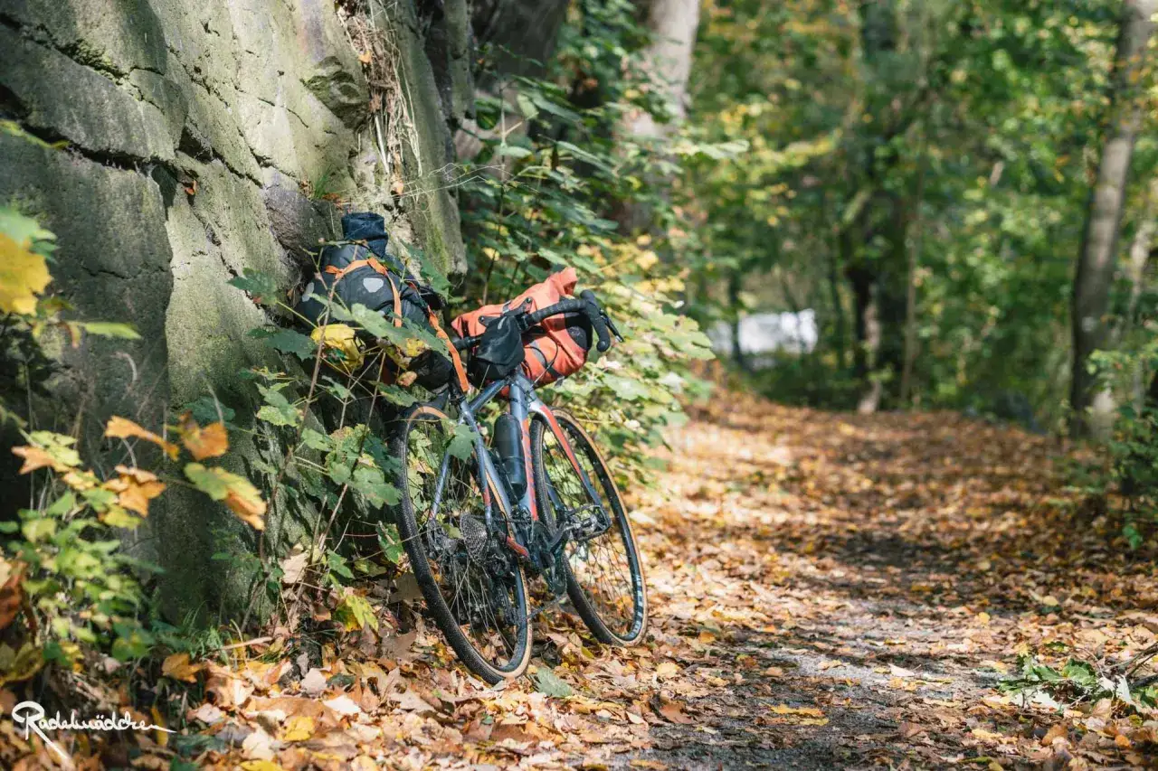 Fahrrad mit Gep&auml;cktaschen lehnt an einer Steinmauer, bereit f&uuml;r e bike touren im Herbstwald.
