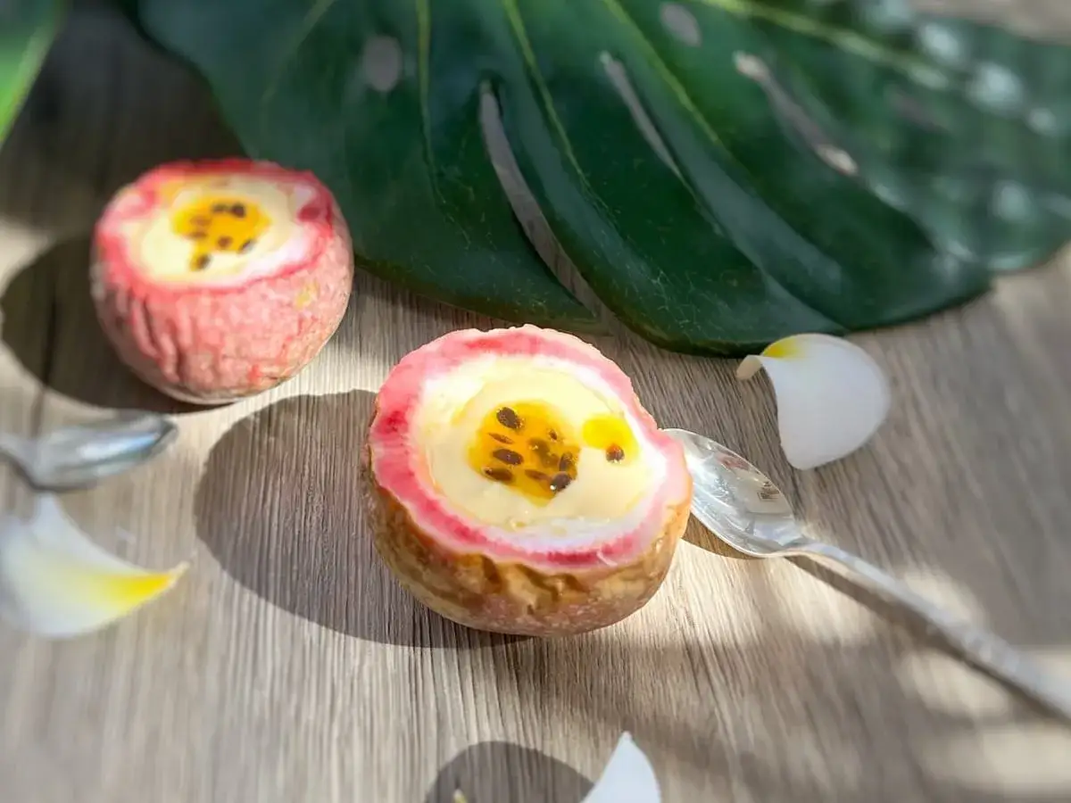 Deux moiti&eacute;s de fruit de la passion garnies d'une cr&egrave;me onctueuse et de leurs p&eacute;pins noirs, sur fond de bois. Une feuille tropicale et des p&eacute;tales de fleurs ajoutent une touche exotique.