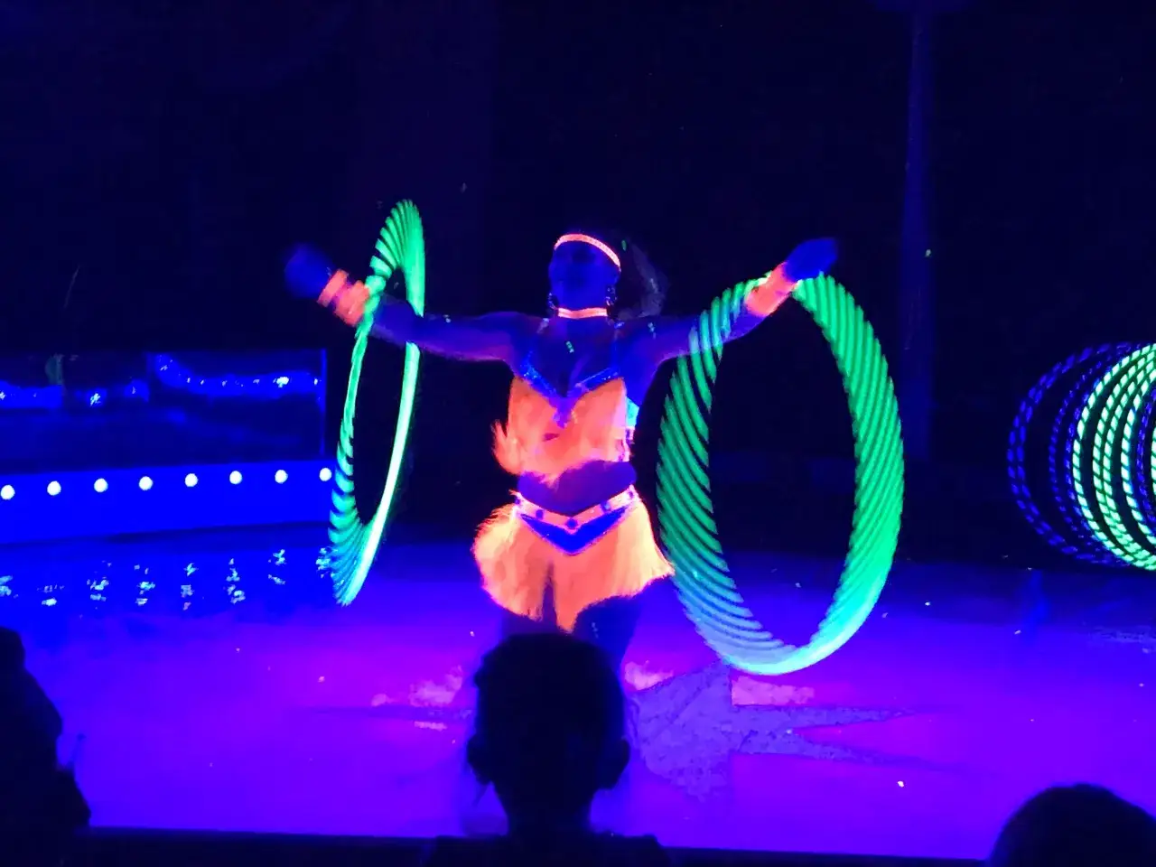 Künstlerin wirbelt leuchtende Reifen im Dunkeln beim Circus Moreno. Neonfarben und Schwarzlicht erzeugen eine magische Atmosphäre.