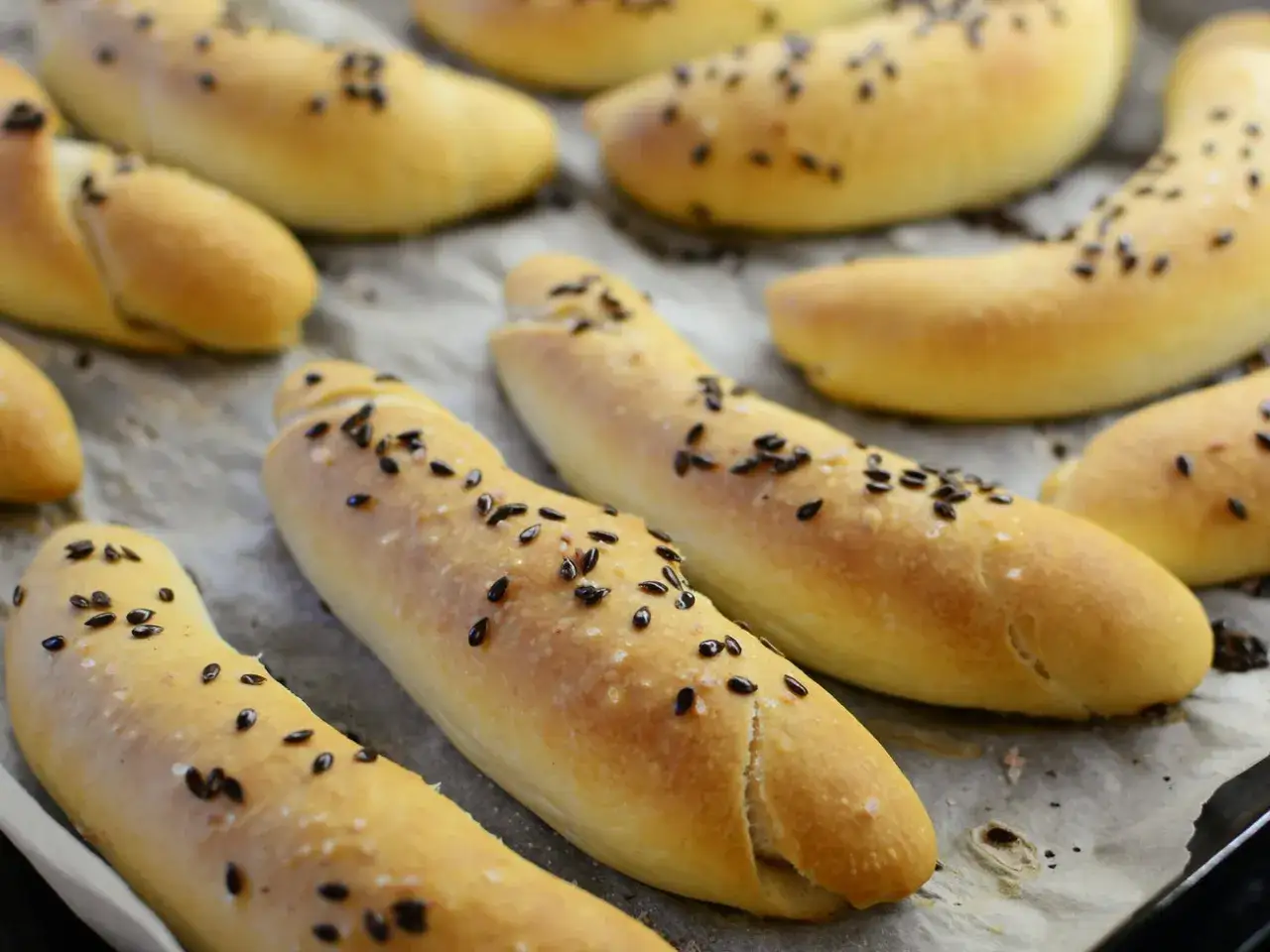 Frisch gebackenes tschechisches Brot, bestreut mit schwarzen Samen und grobem Salz, liegt auf Backpapier.