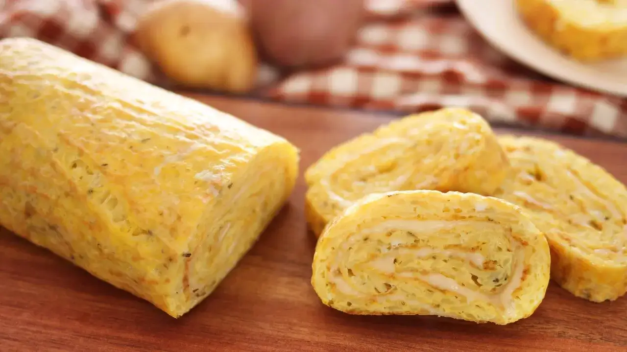 Un rotolo di patate dorato e soffice, tagliato a fette, rivela un ripieno cremoso.