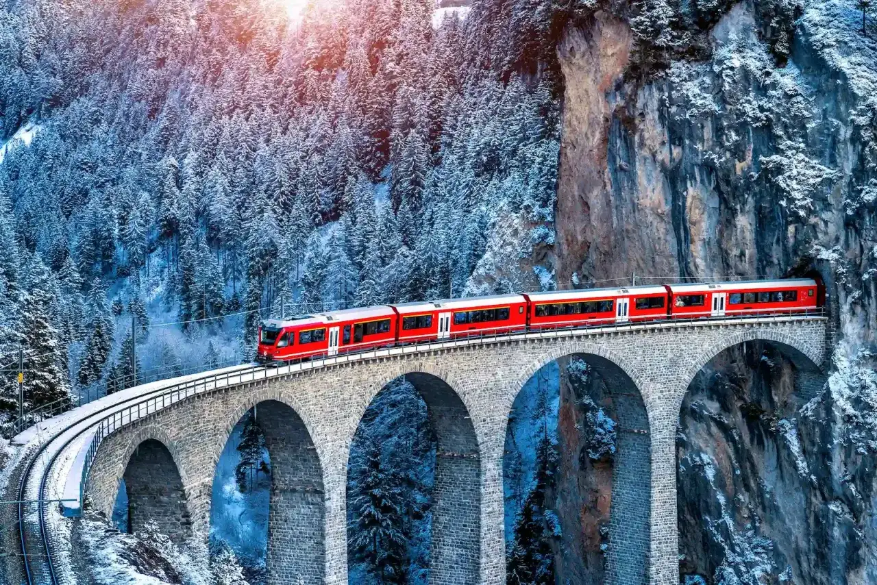 Treno rosso sul viadotto innevato, parte del treno Bernina percorso tra boschi e rocce.