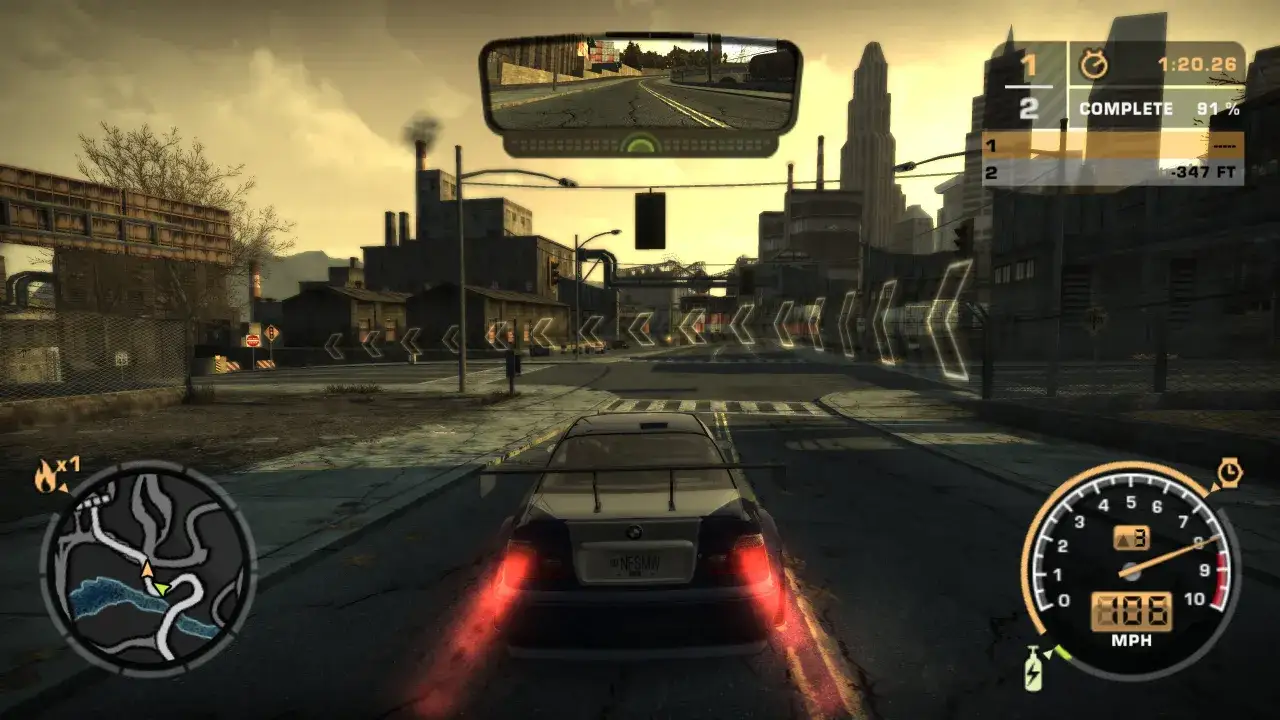 Widok zza kierownicy w grze NFS Most Wanted Redux. Samochód z płonącymi światłami cofania jedzie przez industrialne miasto.
