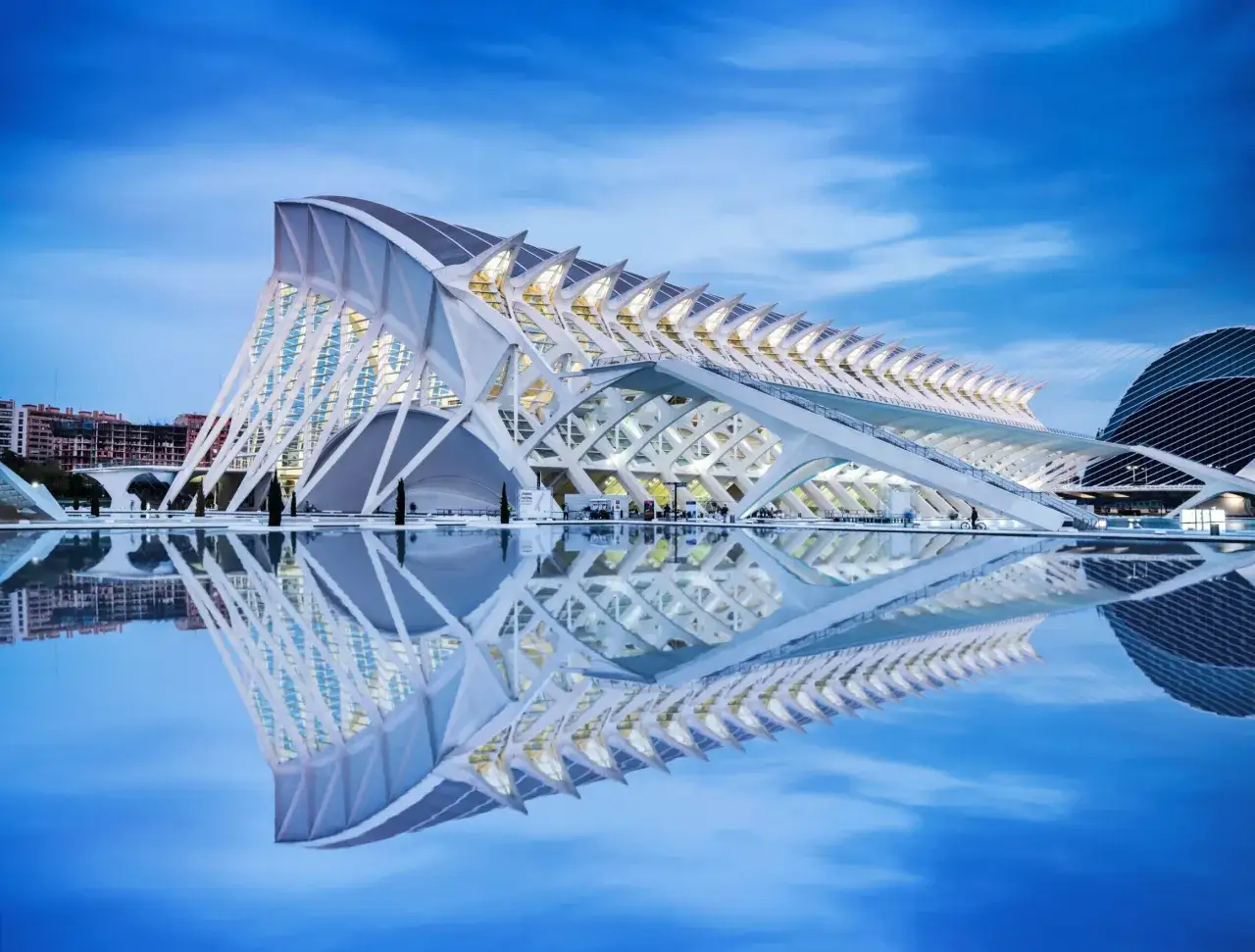 La **Ciudad de las Artes y las Ciencias** de Valencia, con su arquitectura futurista reflejada en el agua, bajo un cielo azul crepuscular.
