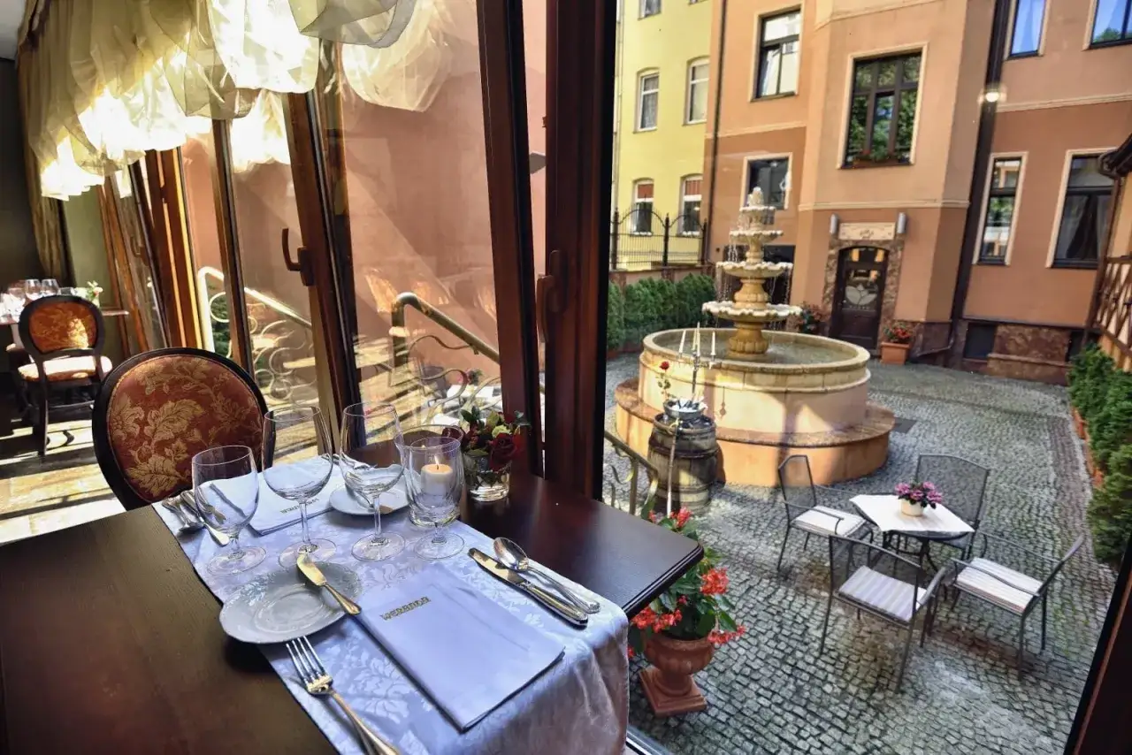 Elegancko nakryty stół w restauracji, z widokiem na urokliwy dziedziniec z fontanną. To z pewnością najlepsza restauracja w Bydgoszczy.