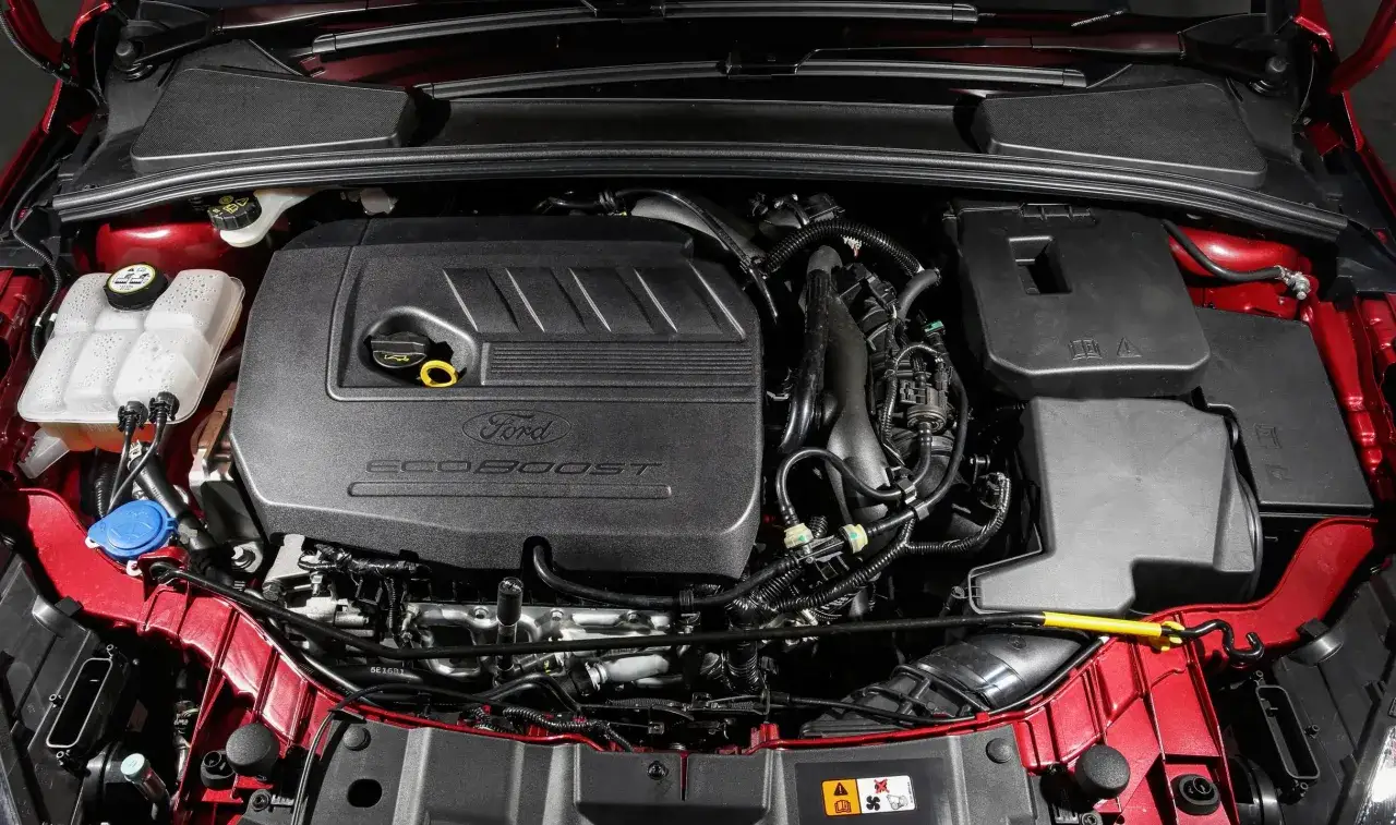 Silnik EcoBoost w Fordzie Focus 2014. Widoczna pokrywa silnika z logo Ford i napisem EcoBoost, przewody i inne elementy komory silnika.