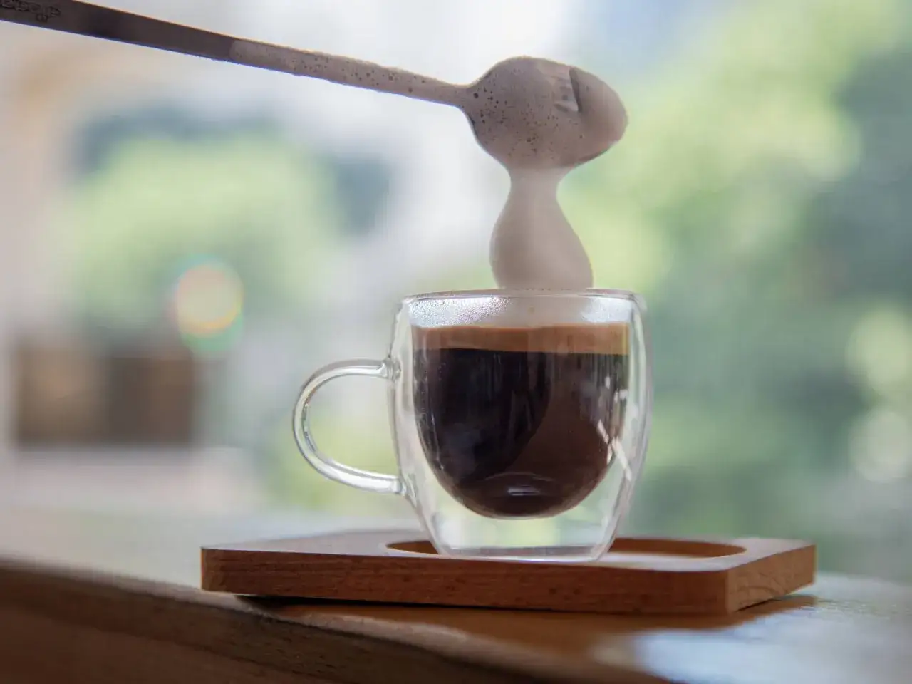 Ein Löffel schäumende Milch wird über einen Espresso Macchiato gegossen.