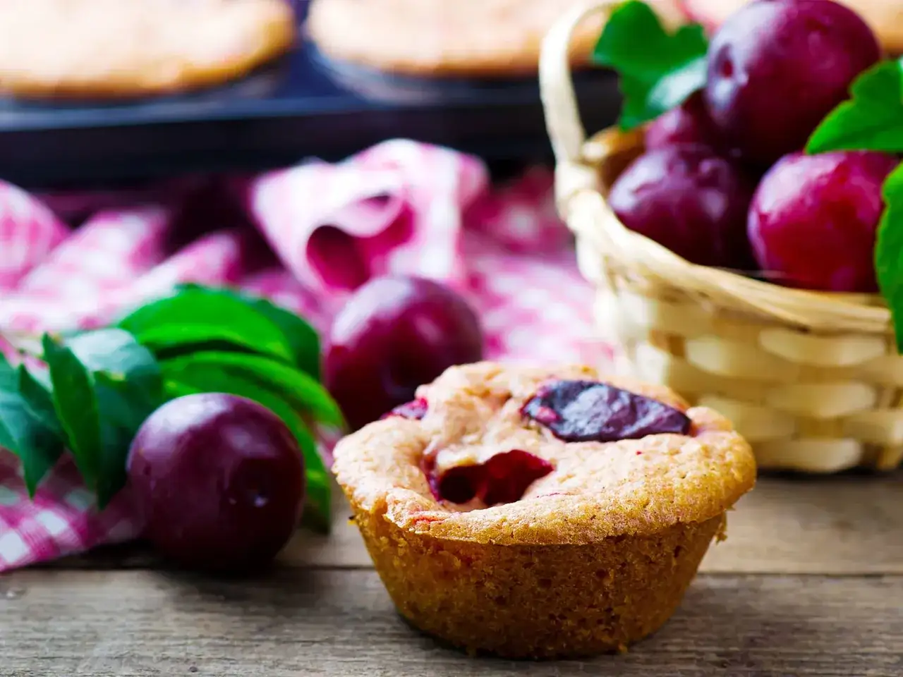 Un d&eacute;licieux muffin aux prunes, avec des prunes fra&icirc;ches dans un panier en osier et sur une serviette &agrave; carreaux.