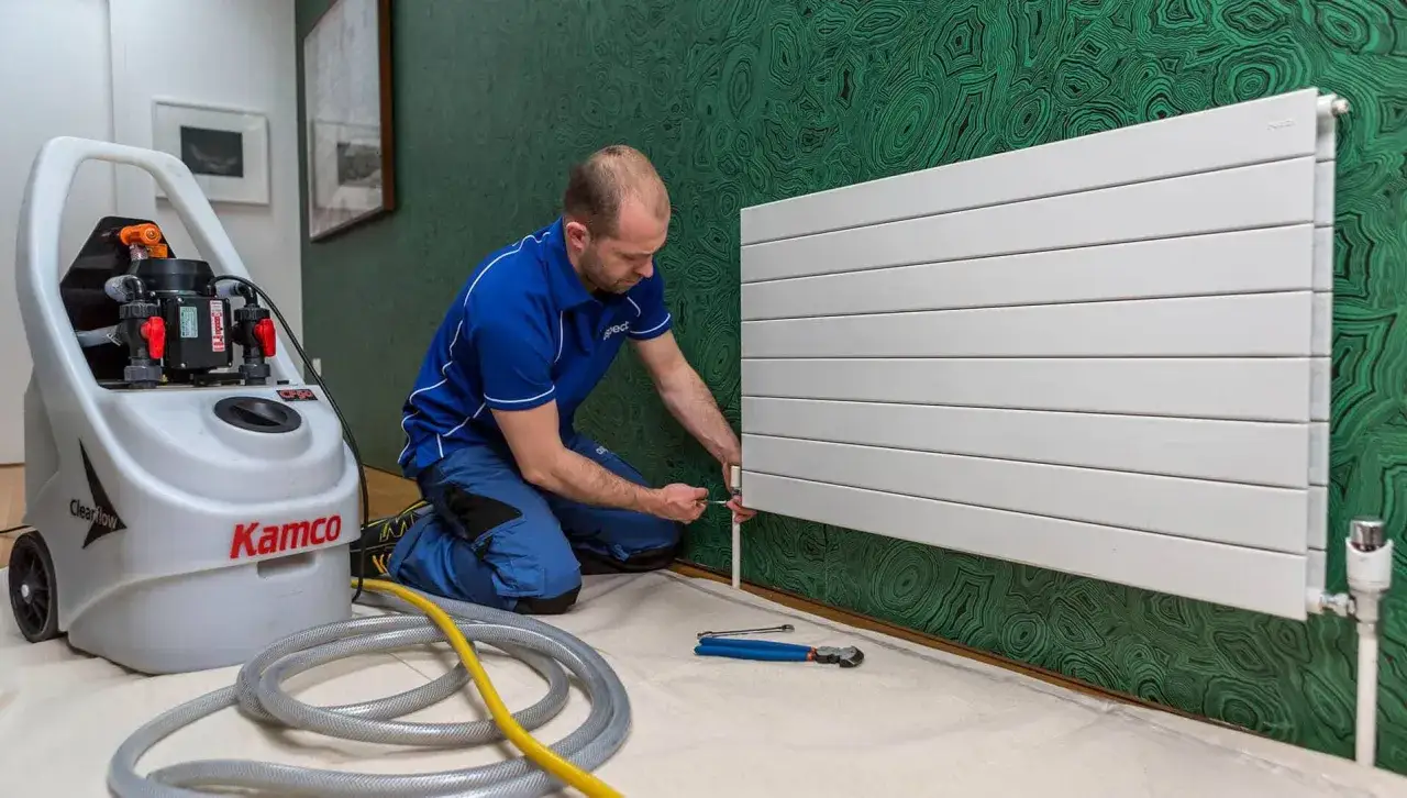 Técnico trabajando en un radiador blanco con una máquina de limpieza. Aprende cómo limpiar radiadores para optimizar tu calefacción.