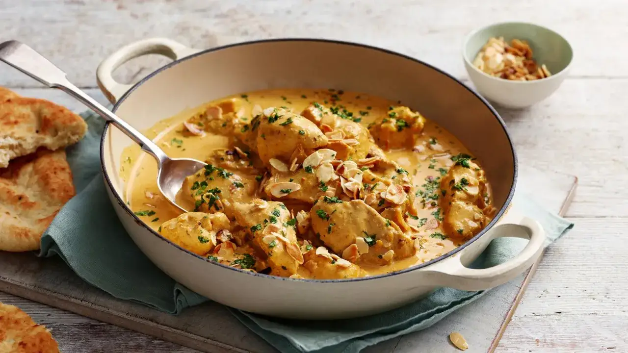 Cremiges Chicken Korma mit Mandelsplittern und frischer Petersilie, serviert in einer Pfanne mit Naan-Brot.