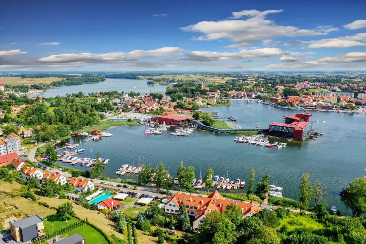 Widok na malowniczą zatokę z licznymi żaglówkami i domkami z czerwonymi dachami. Idealne miejsce, gdzie na Mazury!