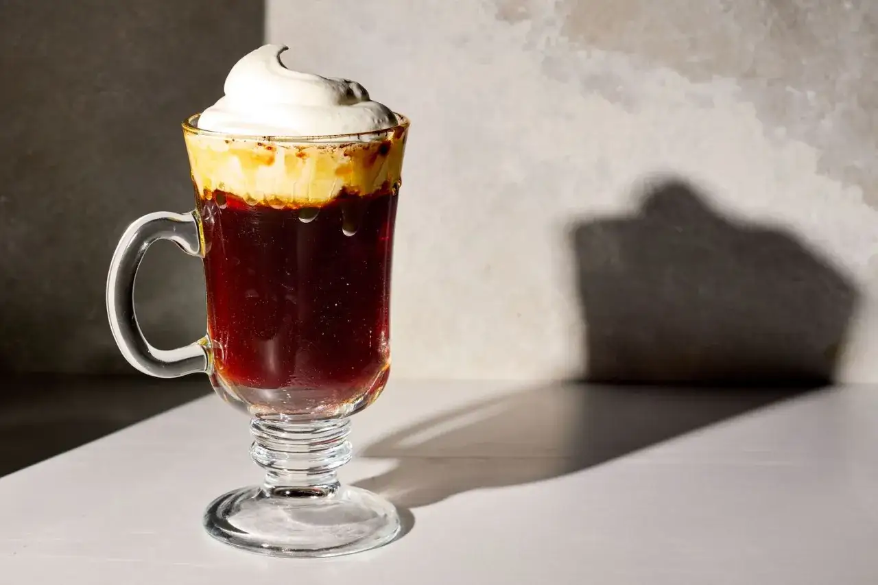 Ett glas med spanskt kaffe, fyllt med mörkt kaffe och toppat med vispad grädde.