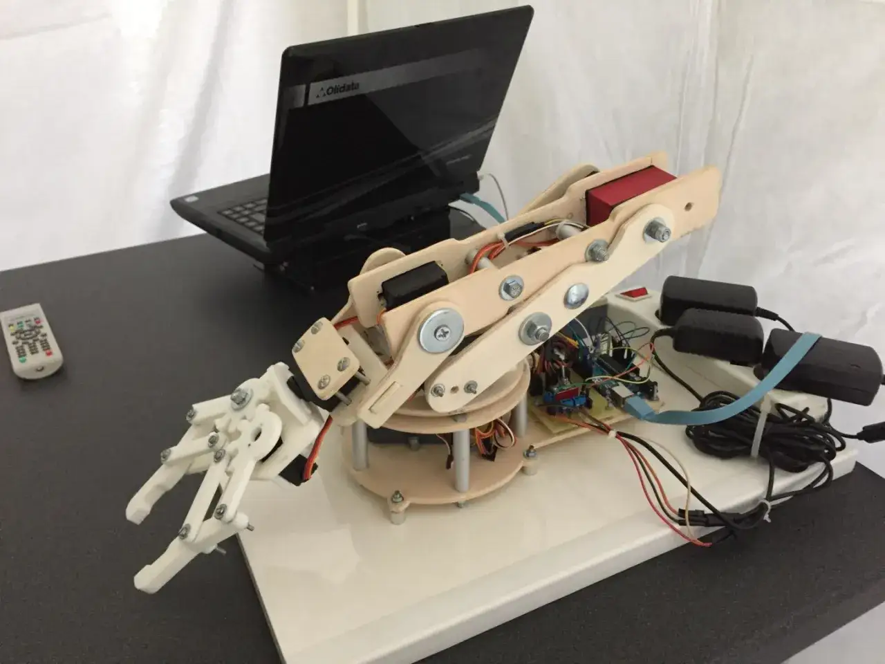 Mano robotica Arduino in legno e plastica, con servomotori e schede elettroniche, collegata a un laptop.