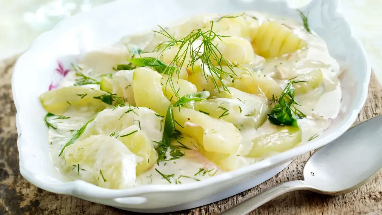 Schmorgurken rezept: Gurkensalat in cremiger Soße mit Dill und Petersilie, serviert in einer weißen Schale.
