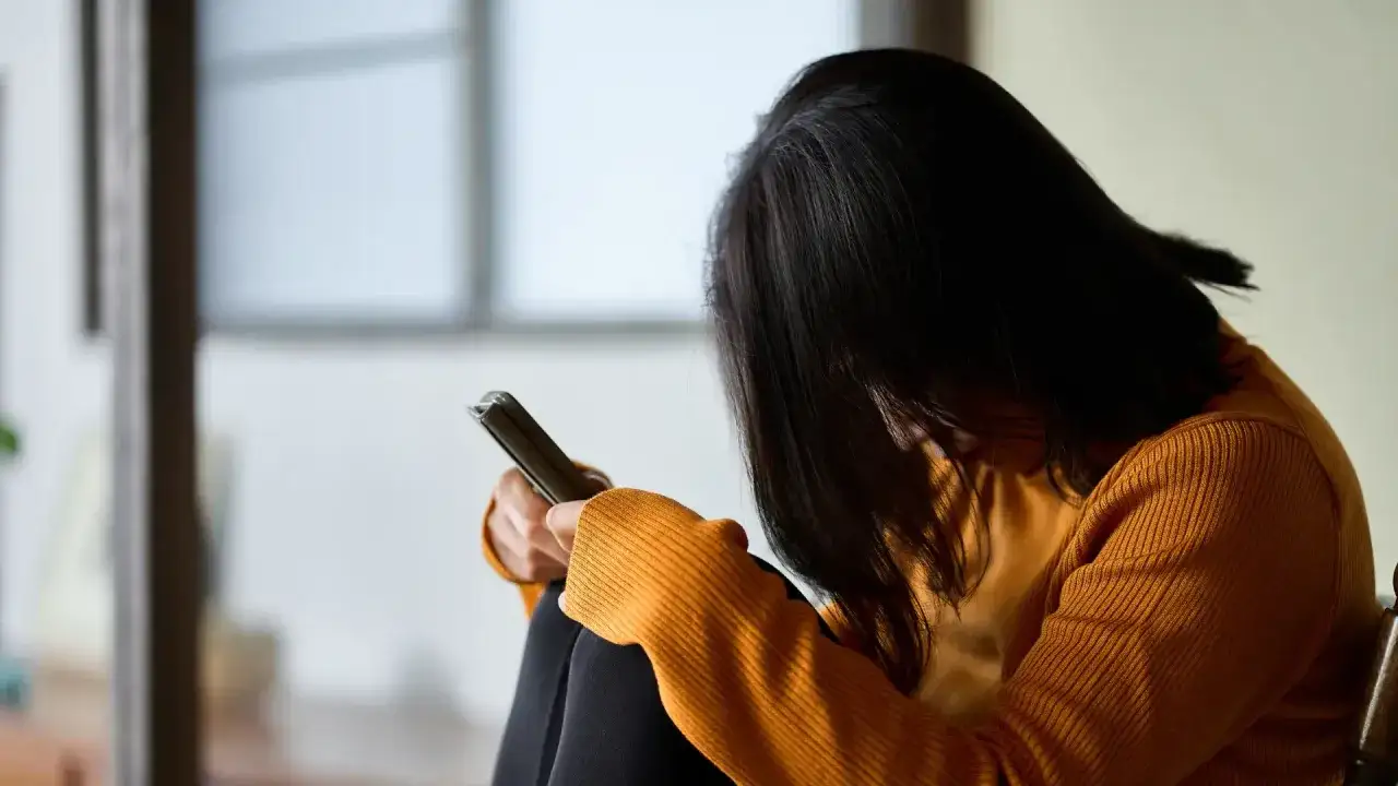 Kobieta z opuszczoną głową przegląda telefon, czując się przygnębiona przez zniesławienie w sieci.
