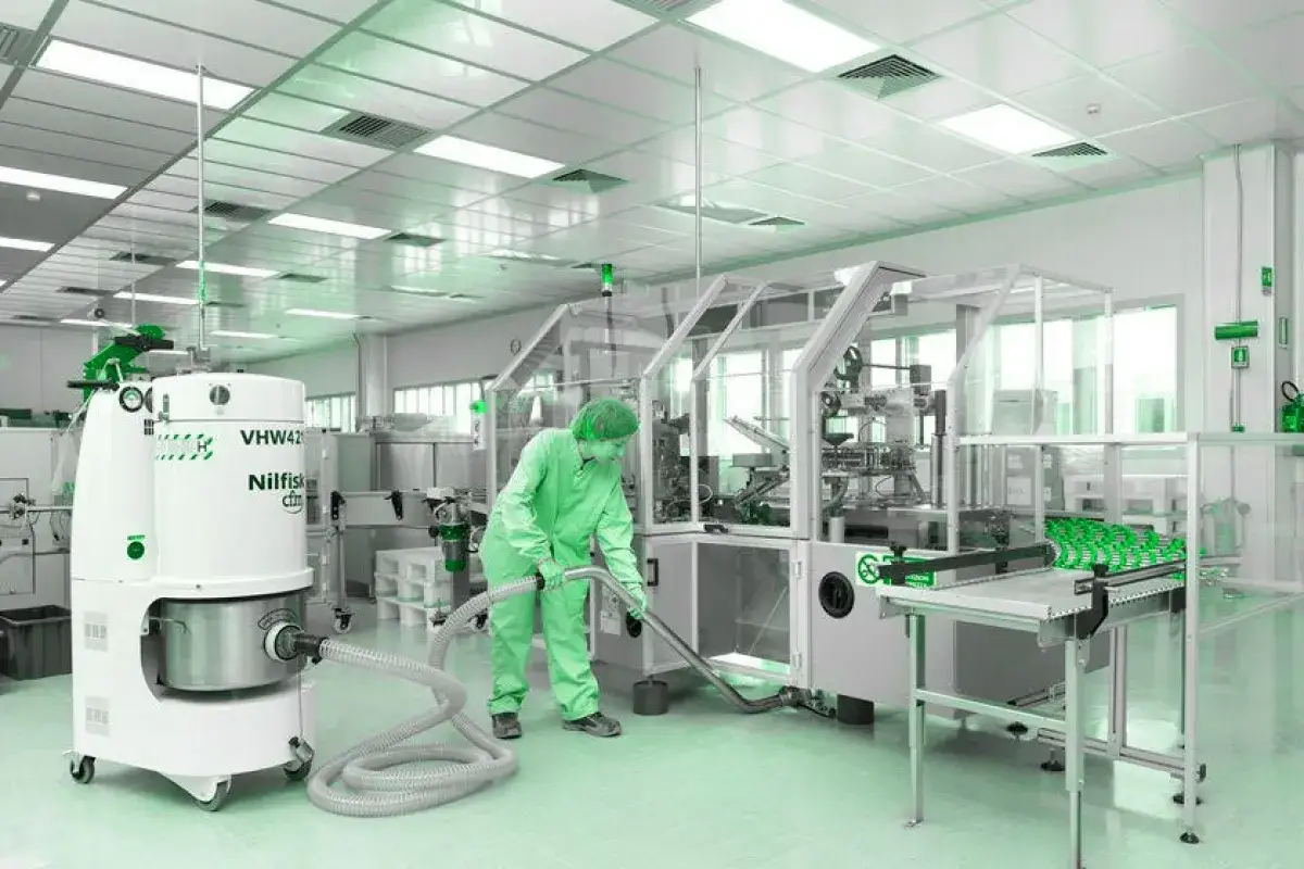 Persona con traje verde y gorro aspira el suelo de un laboratorio limpio, demostrando la asepsia que es fundamental para la producción.