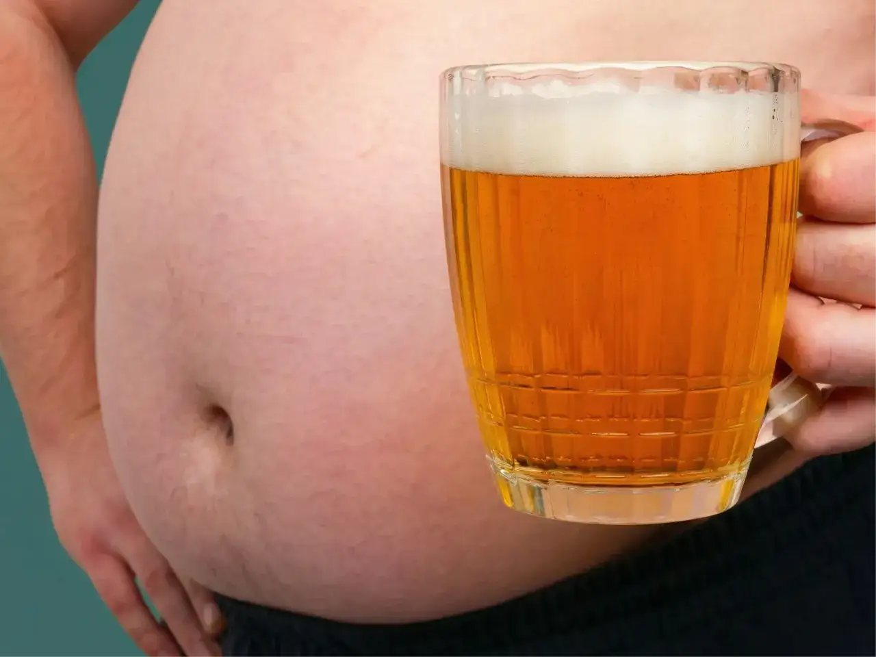 Ein Bierbauch, der zeigt, dass Bier dick macht. Eine Hand hält ein Glas Bier vor einem großen Bauch.