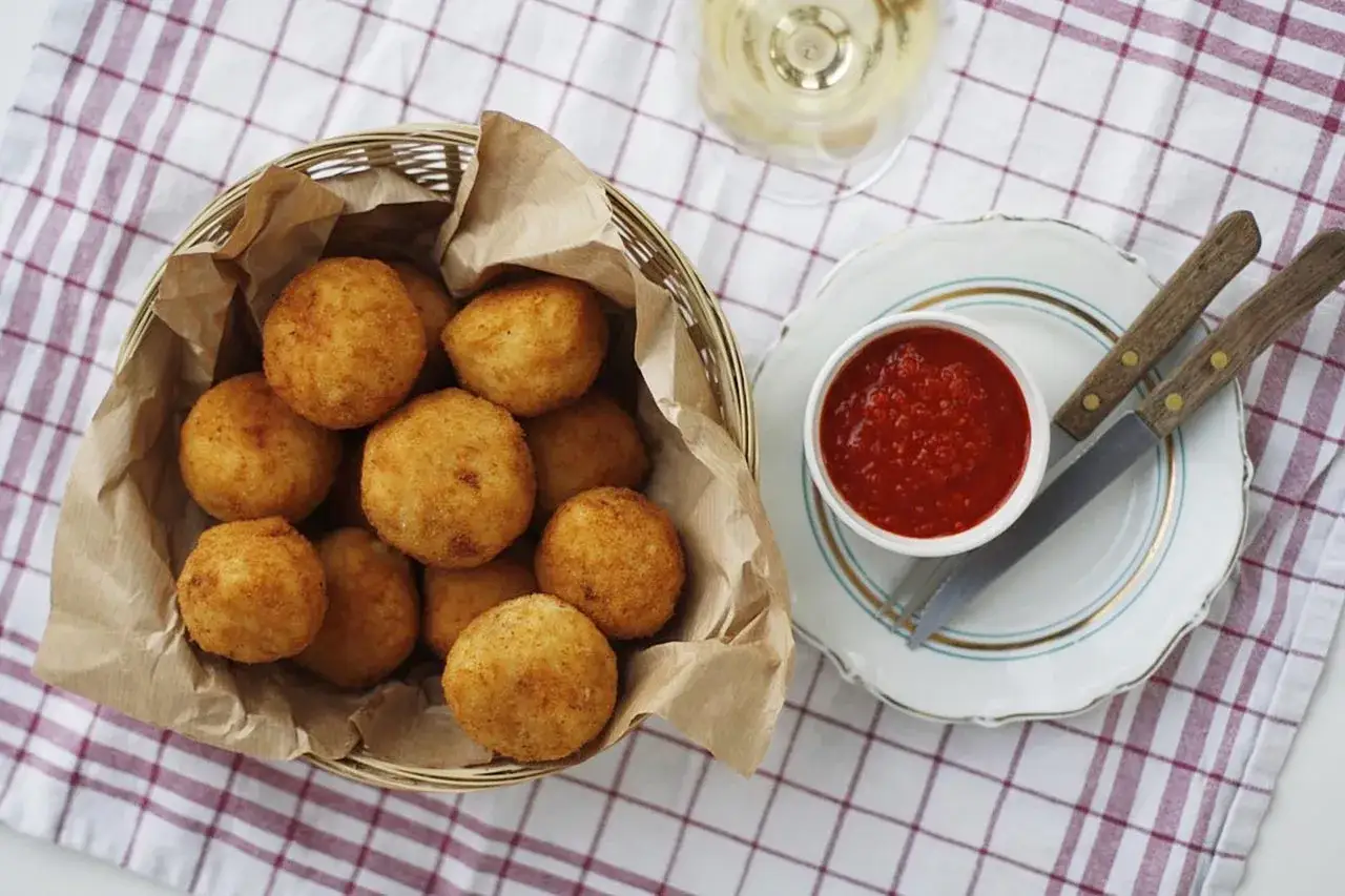 Koszyk pełen złocistych arancini, czyli smażonych kulek ryżowych, z sosem pomidorowym i kieliszkiem białego wina.