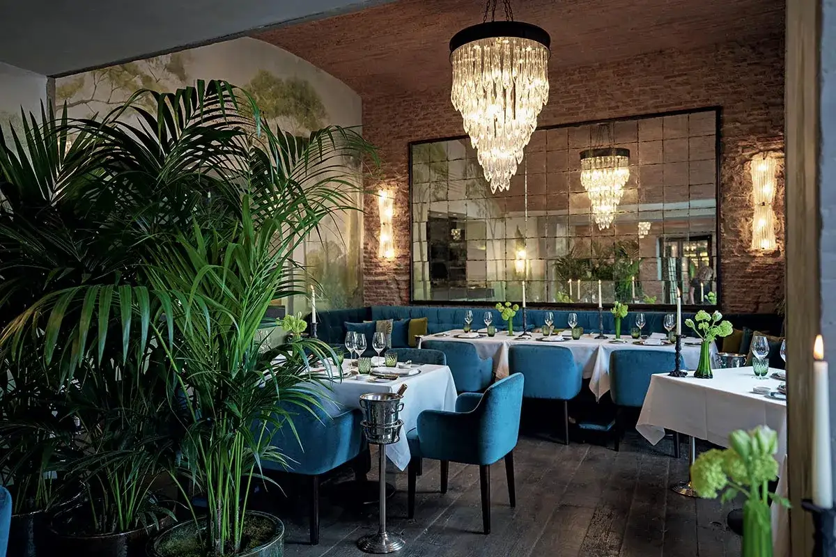 Interno elegante di un ristorante con piante verdi lussureggianti, tavoli apparecchiati e un lampadario scintillante, che evoca l'atmosfera di una stella michelin verde.