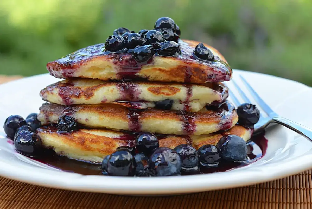 Ein Stapel Buttermilch-Pancakes mit Blaubeersauce und frischen Blaubeeren, serviert auf einem weißen Teller.